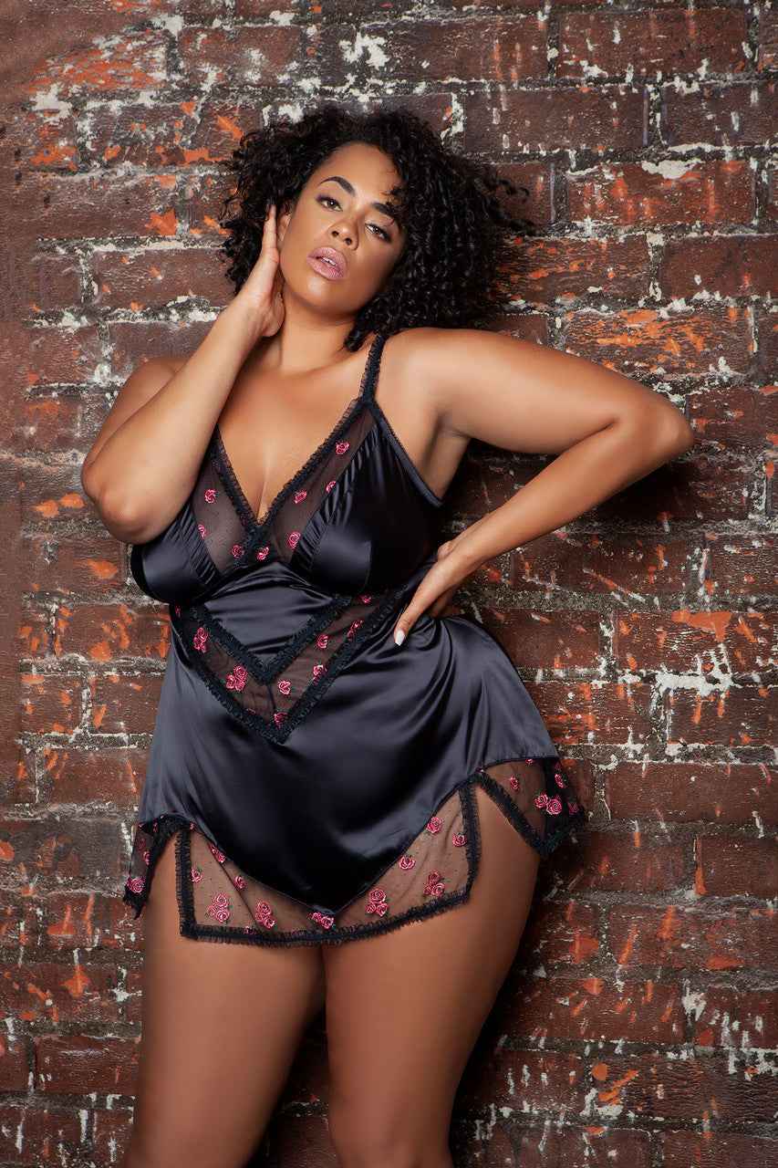Plus size satin babydoll lingerie in black with floral lace details worn by model against brick wall